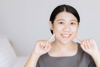 美丽的年轻的亚洲女人白色婴儿脸健康的牙齿手指点脸面部皮肤护理概念