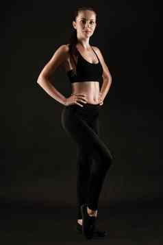 浅黑肤色的女人女人黑色的紧身裤前运动鞋摆姿势黑色的背景健身健身房健康的生活方式概念完整的长度