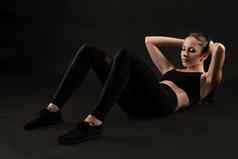 浅黑肤色的女人女人黑色的紧身裤前运动鞋摆姿势黑色的背景健身健身房健康的生活方式概念完整的长度