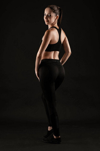 浅黑<strong>肤色</strong>的女人女人黑色的紧身裤前运动鞋摆姿势黑色的背景健身健身房<strong>健康</strong>的生活方式概念完整的长度
