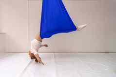 年轻的女人提出了反重力空中瑜伽蓝色的吊床白色背景