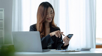 肖像年轻的亚洲业务女人智能手机写笔记本移动PC首页办公室美丽的女孩桌子上电脑首页订单启动业务亚洲女人在线锻造电话销售