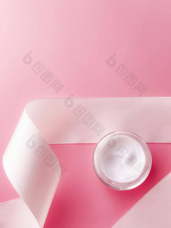 护肤品化妆品脸奶油保湿霜Jar白色丝绸丝带粉红色的背景美产品平铺