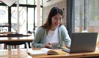 快乐年轻的女人耳机说话移动PC使笔记女孩<strong>学生会</strong>说话的视频会议调用女老师教练辅导网络摄像头在线培训e-coaching概念