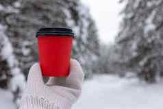 红色的纸杯咖啡手白色针织连指手套背景美丽的冬天森林