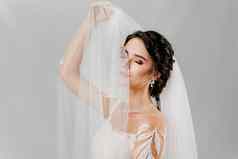 年轻的有吸引力的新娘婚礼衣服触摸新娘面纱白色背景工作室广告社会网络婚礼机构新娘沙龙