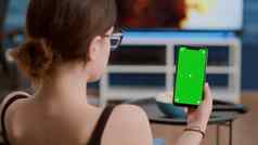 特写镜头年轻的女人持有垂直智能手机绿色屏幕看社会媒体内容