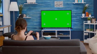 玩家女孩玩控制台视频游戏无线控制器绿色屏幕放松沙发上