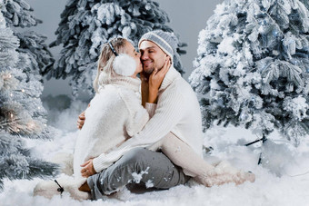 年轻的女人接吻可爱的男人。脸颊冬天假期爱故事年轻的夫妇穿白色套头毛衣快乐男人。年轻的女人拥抱