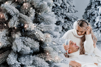 夫妇夫妇笑有趣的雪瀑布圣诞节树冬天假期爱故事年轻的夫妇穿白色套头毛衣快乐男人。年轻的女人拥抱