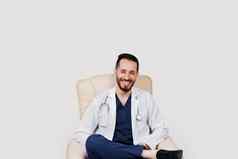 英俊的阿拉伯医生外科医生微笑白色背景有胡子的学生听诊器医疗袍座位扶手椅被冷落的背景
