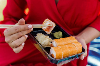 特写镜头寿司集有吸引力的女孩红色的衣服持有寿司筷子手快递交付寿司集漂亮的女人黑色的盒子寿司芥末酱姜