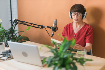 肖像成熟的女人穿耳机会说话的在线广播站播客广播概念