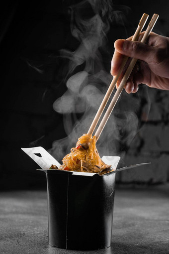 热气腾腾的大米面条锅盒子黑色的背景快食物交付服务外卖中国人街餐乌冬面黑色的食物容器