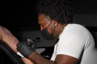 专业非洲美国纹身艺术家使纹身客户端手臂