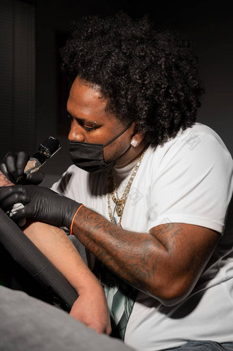 专业非洲美国纹身艺术家使纹身客户端手臂