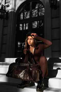 时尚年轻的浅黑肤色的女人女人长腿穿固体长袖bodycon一块连身裤摆姿势皮革棕色（的）旅行袋
