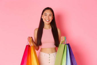 美时尚生活方式概念梦幻时尚的亚洲女孩买假期持有购物袋很高兴微笑站粉红色的背景