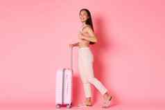 旅行假期假期概念微笑有吸引力的亚洲女孩旅游夏天衣服显示竖起大拇指走粉红色的背景手提箱享受旅程