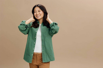 快乐微笑亚洲学生年轻的女人卡其色绿色衬衫触摸头发摆姿势孤立的米色柔和的工作室背景很酷的时尚提供生活方式情绪概念复制空间