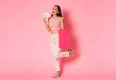 完整的长度无忧无虑的梦幻亚洲美丽的女孩享受购物一天购物中心商店持有商店袋夏天衣服钱站乐观的粉红色的背景
