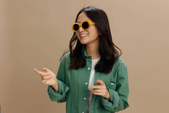 笑快乐朝鲜文年轻的女人卡其色绿色衬衫时尚的眼镜点手指复制空间摆姿势孤立的米色柔和的工作室背景很酷的时尚提供太阳镜概念