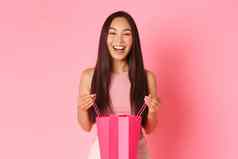 美时尚生活方式概念华丽的快乐亚洲女孩收到礼物持有购物袋微笑梦幻感激好奇的内部站粉红色的背景