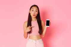 技术沟通在线生活方式概念感兴趣好奇的亚洲女孩想知道问题移动电话应用程序指出智能手机屏幕粉红色的背景