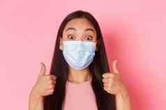 科维德流感大流行冠状病毒社会距离概念特写镜头兴奋惊讶漂亮的亚洲女孩支持伟大的的想法赞美不错的选择赞美显示竖起大拇指穿医疗面具