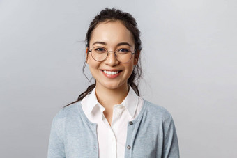 特写镜头肖像有吸引力的友善的亚洲女办公室工人员工老师眼镜微笑广泛的相机热情的的态度站灰色背景