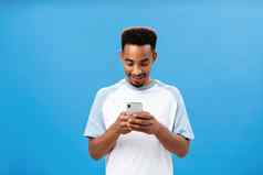 皮肤黝黑的的家伙发短信太棒了女孩约会应用程序持有智能手机手机屏幕娱乐逗乐表达式玩很酷的应用程序站蓝色的背景