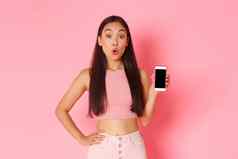 技术沟通在线生活方式概念感兴趣好奇的亚洲女孩想知道问题移动电话应用程序指出智能手机屏幕粉红色的背景