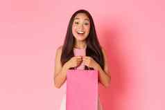 美时尚生活方式概念华丽的快乐亚洲女孩收到礼物持有购物袋微笑梦幻感激站粉红色的背景