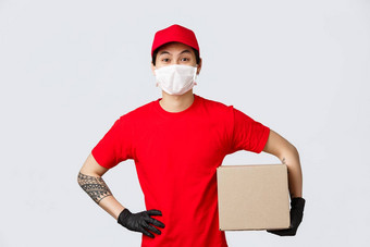 快乐的亚洲男人。红色的帽t恤持有包裹盒子穿保护手套医疗面具快递拾音器包客户端航运盒子科维德流感大流行爆发