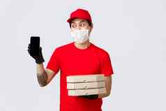 有趣的交付的家伙红色的帽t恤持有披萨盒子显示智能手机屏幕亚洲快递确认订单信息客户端带食物人首页检疫穿医疗面具