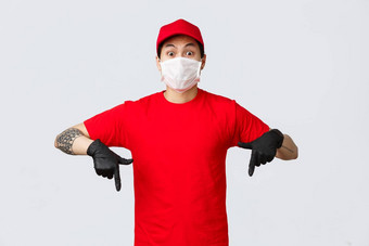 惊讶兴奋亚洲交付的家伙红色的统一的帽t恤表达冲击情绪眼睛指出手指保护手套医疗面具显示促销提供