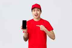 交付应用程序在线购物航运概念惊讶亚洲快递红色的帽t恤指出手指移动电话应用程序显示智能手机屏幕逗乐脸