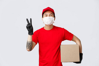 概念交付冠状病毒流感大流行快乐的微笑亚洲快递红色的帽t恤显示和平标志持有包裹穿医疗面具手套客户端安全交付包