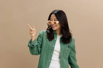 笑快乐朝鲜文年轻的女人<strong>卡其色</strong>绿<strong>色</strong>衬衫时尚的眼镜点手指复制空间摆姿势孤立的米<strong>色</strong>柔和的工作室背景很酷的时尚提供太阳镜概念