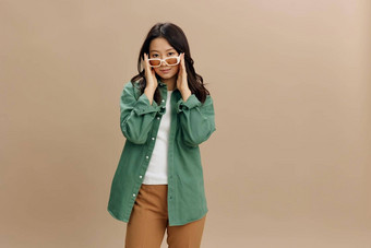 可爱的朝鲜文微笑年轻的女人<strong>卡其色</strong>绿<strong>色</strong>衬衫时尚的触摸眼镜摆姿势孤立的米<strong>色</strong>柔和的工作室背景很酷的时尚提供太阳镜概念