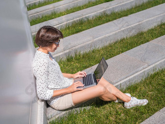 女人坐在移动PC城市公园板凳上自由职业者工作学生学习远程在户外现代生活方式夏天共鸣户外工作场所