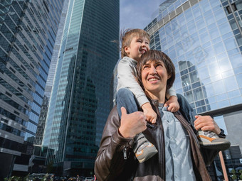 男孩坐在父亲的肩膀摩天大楼爸爸儿子玻璃墙建筑未来现代技术生活平衡家庭生活区