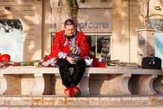 sliema马耳他2月音乐家智能手机坐着板凳上男人。色彩斑斓的服装准备好了晚上狂欢节