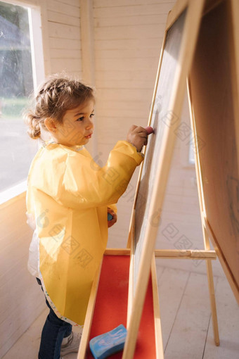 年轻的艺术家油漆木董事会粉笔可爱的女孩的大楼雨衣