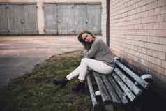 女人坐着破旧的板凳上白色裤子灰色的针织毛衣黑色的靴子