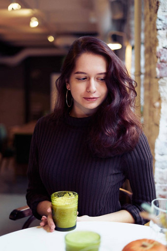 美丽的时尚的时尚聪明的女孩坐着咖啡馆喝健康的绿色黄色的奶昔拿铁素食主义者迷人的深思熟虑的女人长黑暗棕色（的）头发