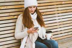 美丽的年轻的女孩喝咖啡茶塑料杯子秋天冬天会说话的移动电话女人长头发坐着板凳上秋天冬天姥热喝复制空间
