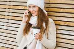 美丽的年轻的女孩喝咖啡茶塑料杯子秋天冬天会说话的移动电话女人长头发坐着板凳上秋天冬天姥热喝复制空间