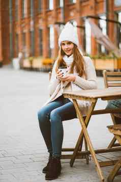 美丽的年轻的女孩喝咖啡茶塑料可重用的杯子秋天冬天女人长头发温暖的衣服坐着街咖啡馆温暖热喝垂直