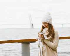 美丽的年轻的女孩喝咖啡茶塑料杯子秋天冬天女人长头发站海滨波罗的海海港口等待渡船加热热喝复制空间